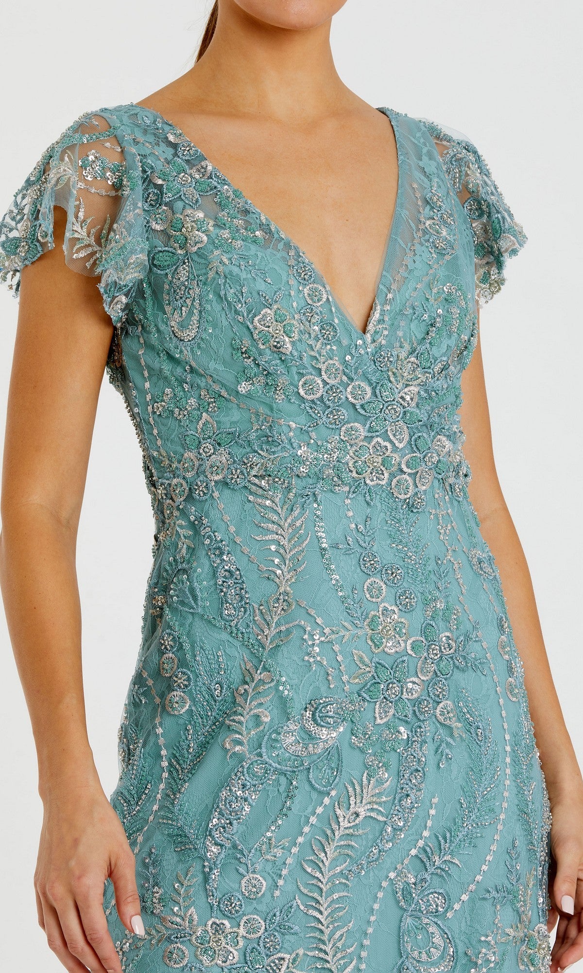 A woman wears the Mac Duggal 68914 Long Formal Dress—a teal gown with short sleeves and a V-neckline, adorned with intricate silver bead and sequin embroidery over delicate lace fabric.